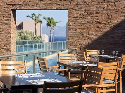 Leeres Restaurant mit Holztischen und Stühlen, Blick auf Meer und Palmen durch Fenster.