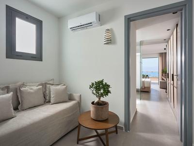 Helles Wohnzimmer mit grauer Couch, Holztisch und grüner Pflanze, Blick in Flur und Schlafzimmer.