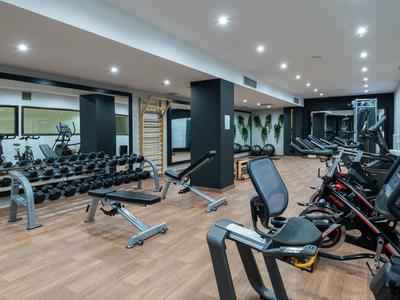 Moderner Fitnessraum mit Hanteln, Trainingsmaschinen und Holzbodenbeleuchtung.