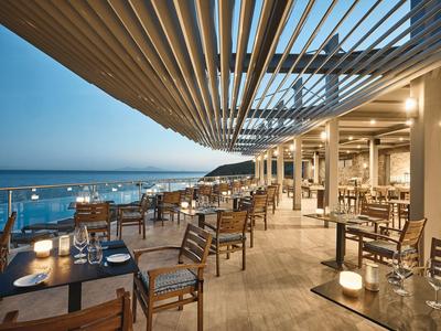 Offenes Restaurant mit Holzstühlen und Tischen am Meer bei Sonnenuntergang, modern und gemütlich.