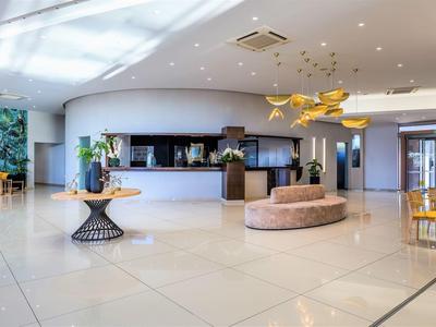 Heller, moderner Hotellobby mit rundem Empfangstresen, beiger Sitzbank und goldenen Pendelleuchten.