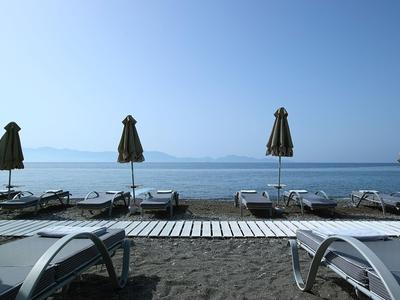 Strand mit Liegestühlen und geschlossenen Sonnenschirmen vor ruhigem Meer und klarem Himmel.