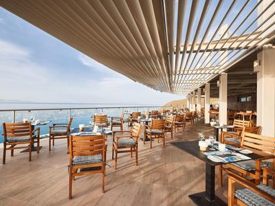 Große Dachterrasse mit Holzstühlen und Tischen, Glasgeländer und modernem Sonnenschutz.