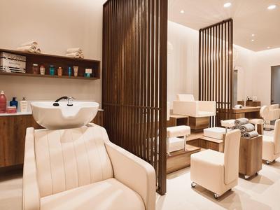 Moderner Friseursalon mit beigen Ledersesseln, Holzregalen und Trennwänden aus dunklem Holz.