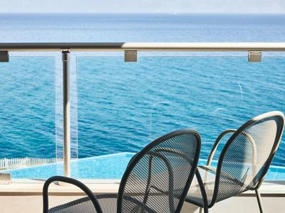 Zwei Metallstühle auf einem Balkon mit Glasgeländer über ruhigem, blauem Meer.