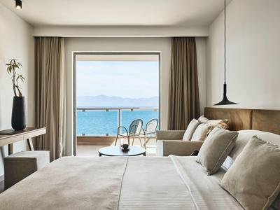 Helles Zimmer mit großem Bett, Sofa, Holzdekor und Balkon mit Meerblick bei klarem Himmel.