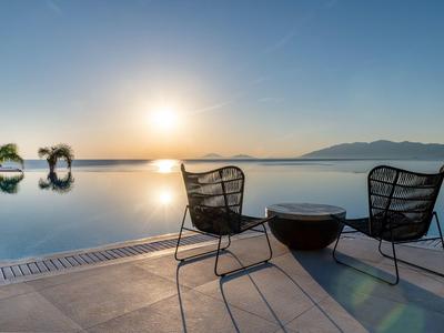 Zwei schwarze Stühle und ein Tisch stehen am Pool, Sonnenuntergang über Bergen und klarem Himmel.