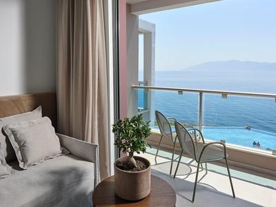 Balkon mit Meerblick, zwei Metallstühlen, Pflanze auf Holztisch und Couch mit Kissen im Zimmer.
