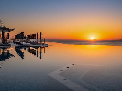 Ruhe am Pool mit klarer Wasseroberfläche und Sonnenuntergang am Horizont.