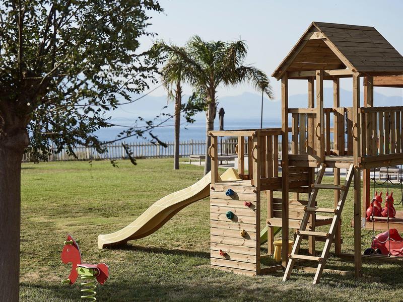 Parco giochi per bambini con struttura da arrampicata e scivolo in un parco con vista sul mare.