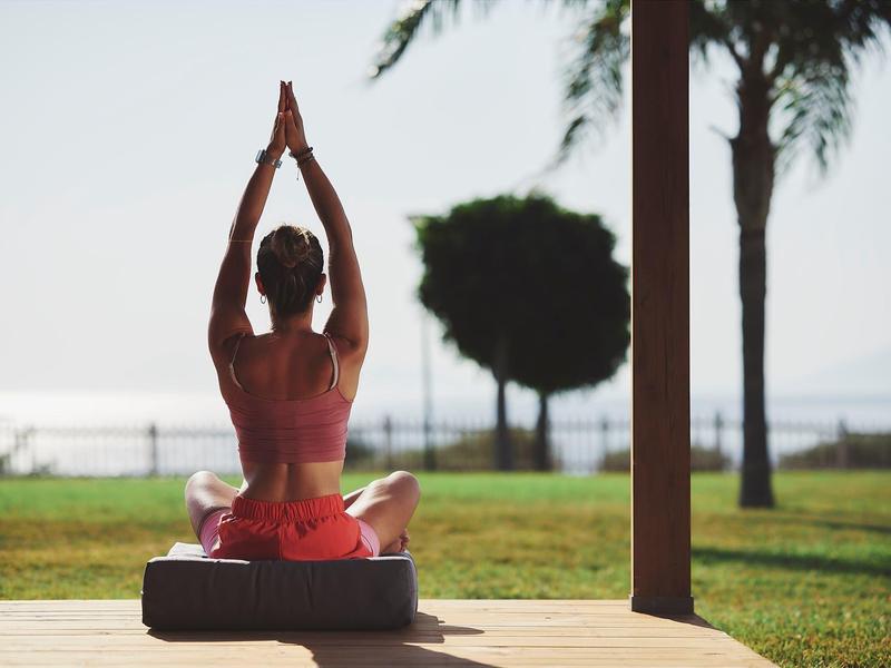 Donna che pratica yoga all'aperto su un tappetino con vista su giardino e acqua.