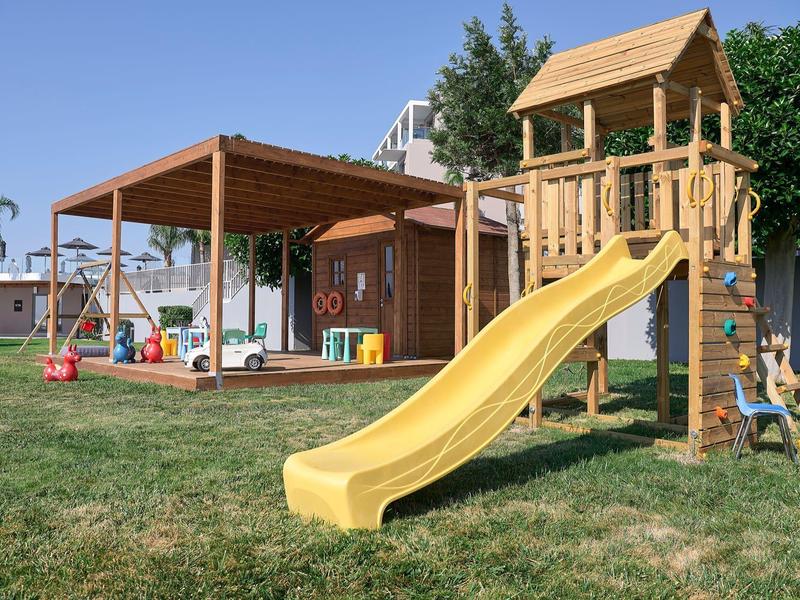 Parco giochi con scivolo giallo e area coperta su prato verde sotto cielo sereno