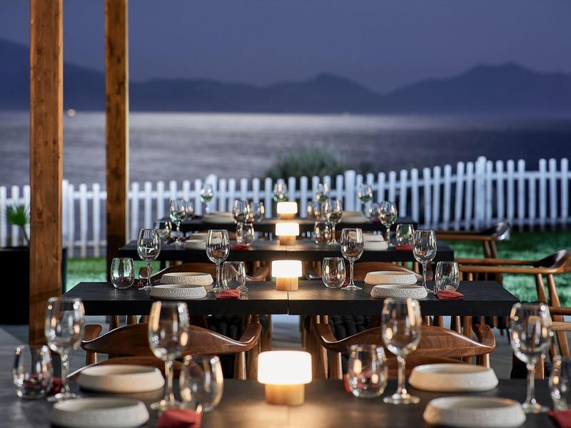 Cena elegante su una terrazza con vista su acqua calma e montagne sullo sfondo.