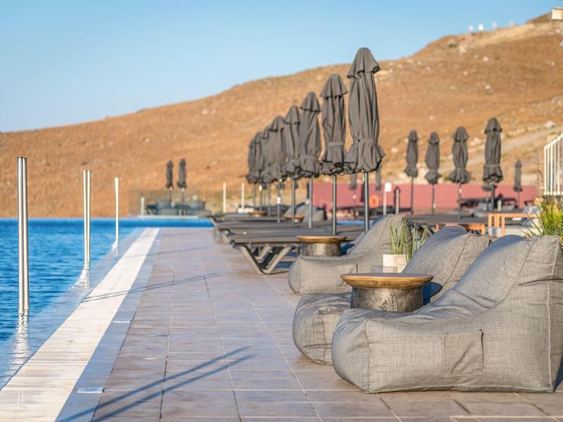 Sedili lounge moderni e ombrelloni chiusi vicino alla piscina con paesaggio collinare sotto un cielo sereno.