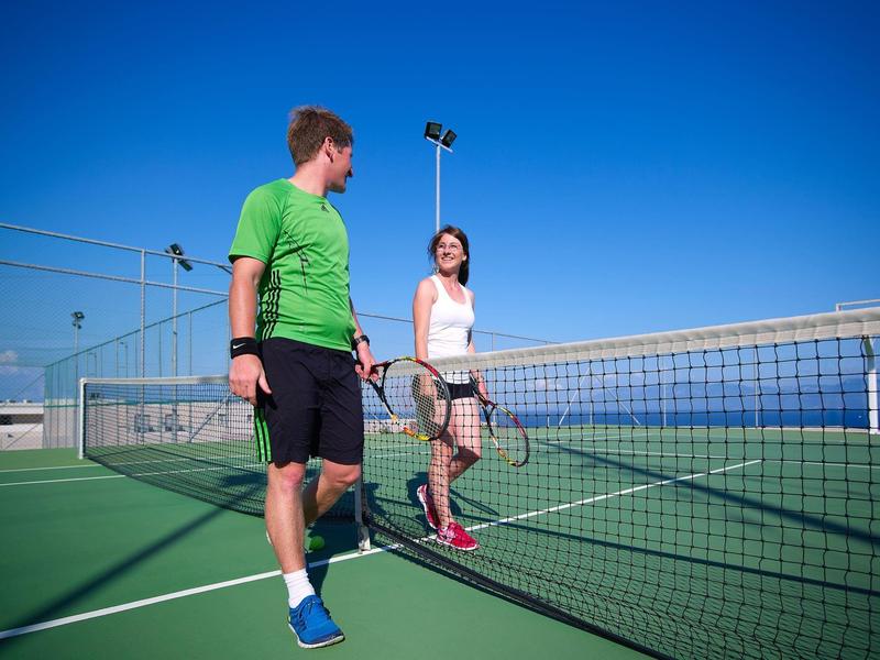 Due persone sono in piedi su un campo da tennis accanto alla rete sotto un cielo azzurro.