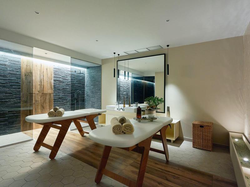 Area spa moderna con due lettini da massaggio, grandi specchi e illuminazione rilassante.