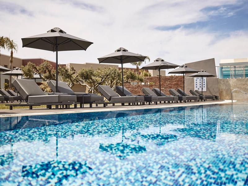 Piscina esterna moderna con lettini e grandi ombrelloni sotto un cielo parzialmente nuvoloso.