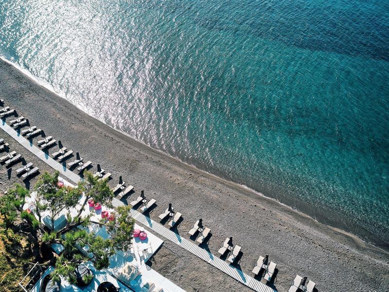 Veduta aerea di una spiaggia di ciottoli con lettini e acqua blu cristallina.