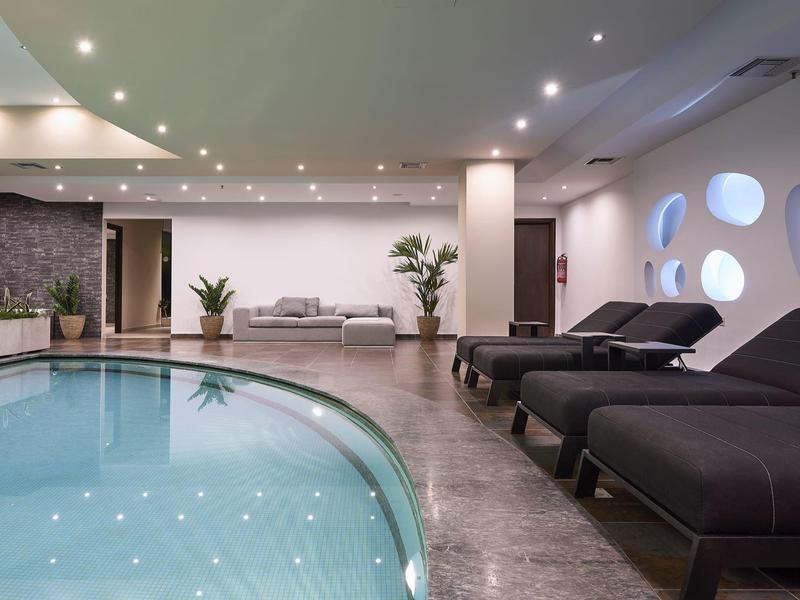 Piscina interna moderna con comodi lettini e illuminazione elegante in un hotel.