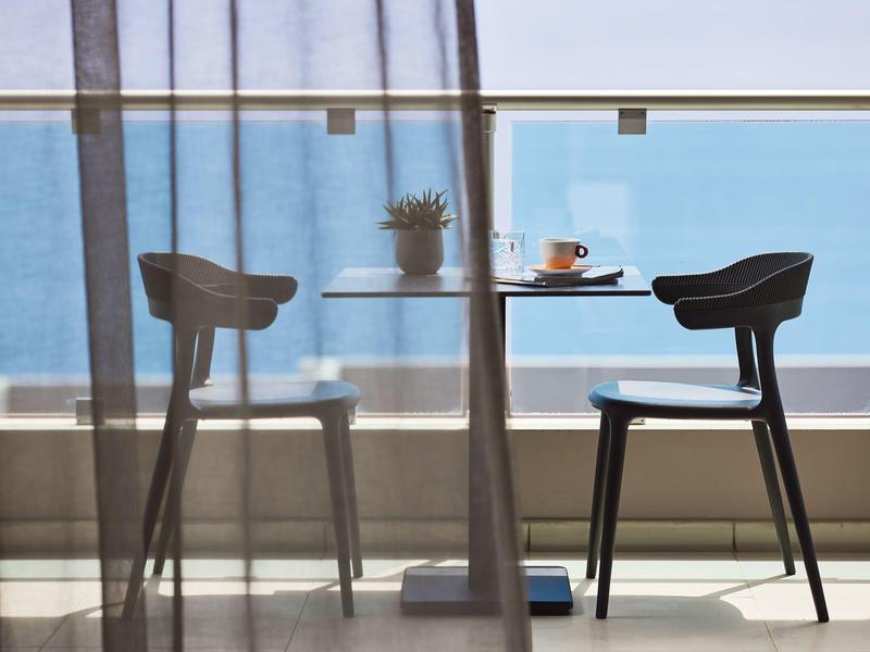 Balcone moderno con tavolo, due sedie e vista chiara sul mare.