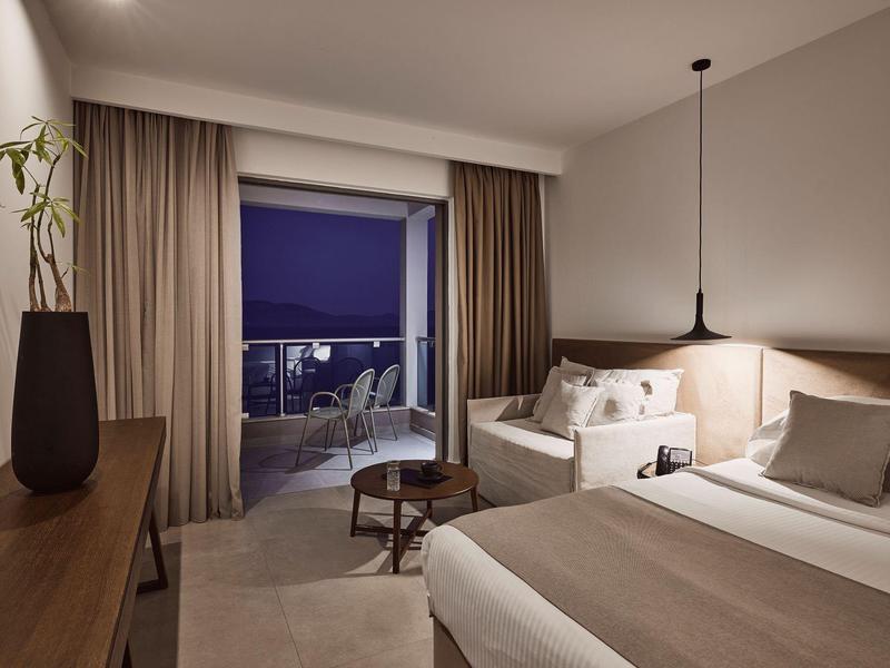 Camera d'hotel accogliente con letto, divano, lampade da comodino e balcone con vista notturna.