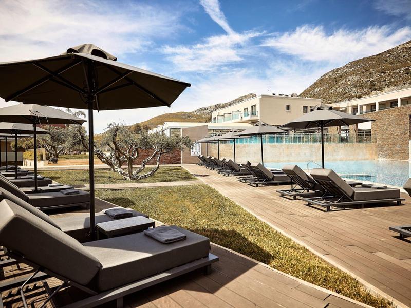 Lettini moderni con ombrelloni accanto a una piscina all'aperto in un hotel sotto un cielo blu.