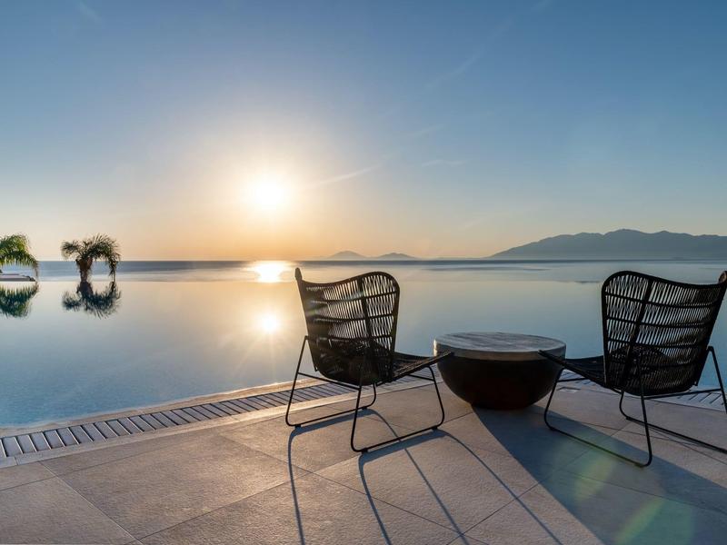Due sedie e un tavolo vicino alla piscina con vista sul tramonto sul mare.