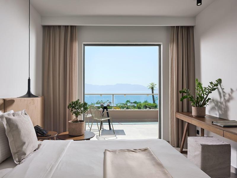 Camera da letto moderna con grandi finestre, vista mare, biancheria bianca e piante.