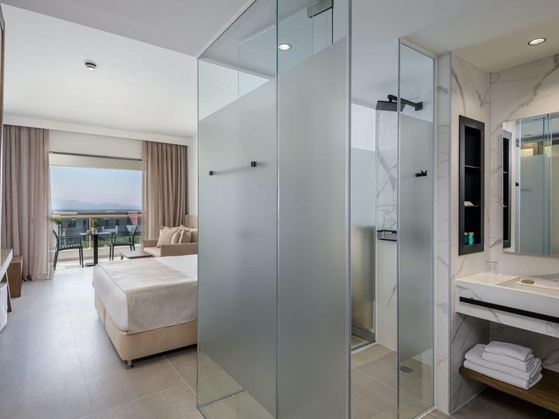 Camera d'hotel moderna con letto e bagno adiacente con doccia e lavabo.