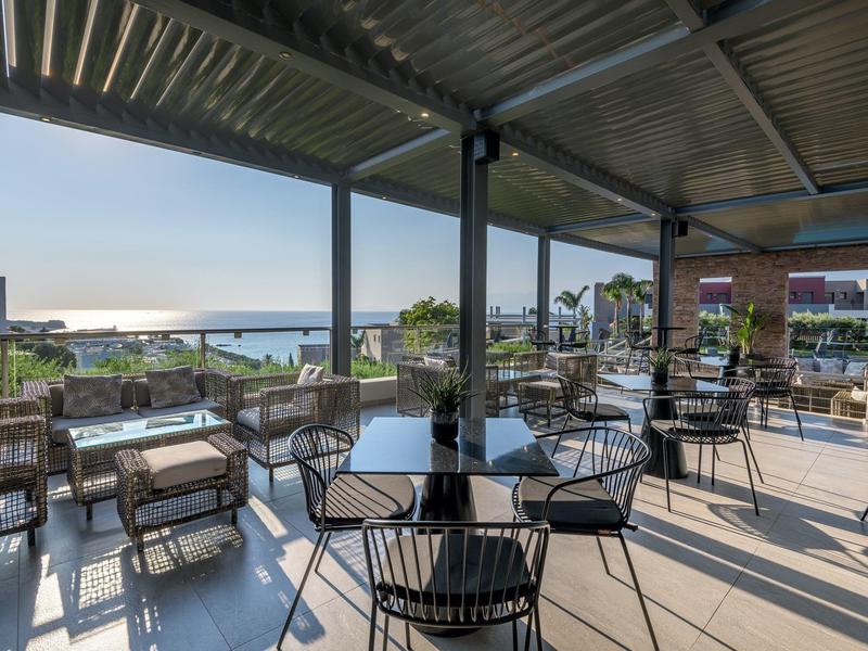 Terrazza esterna coperta con sedie e tavoli con vista sul mare al tramonto.