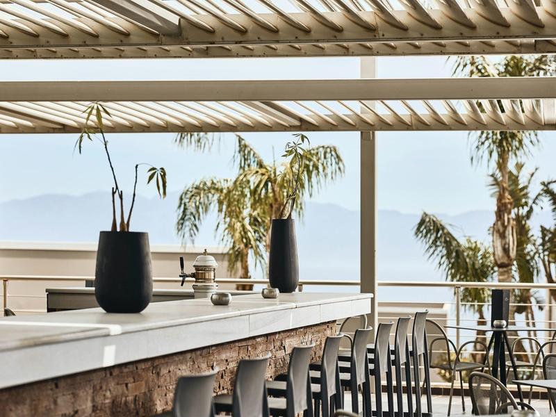 Terrazza moderna dell'hotel con bar, sgabelli alti, piante e vista mare