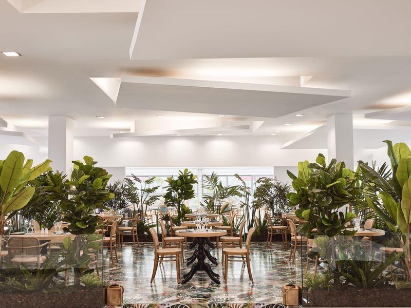 Ristorante moderno in hotel con piante, tavoli e sedie in uno spazio luminoso e aperto