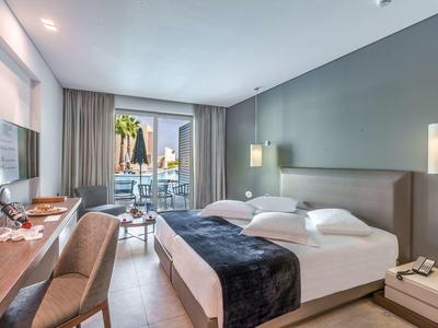 Modernes Hotelzimmer mit Doppelbett, Schreibtisch, Fernseher und Balkon mit Stadtblick.