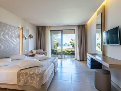 Modern hotel room with double bed, seating area, and view of terrace overlooking the sea.