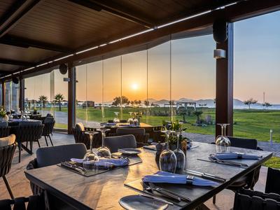 Open restaurant area with set tables overlooking a meadow at sunset