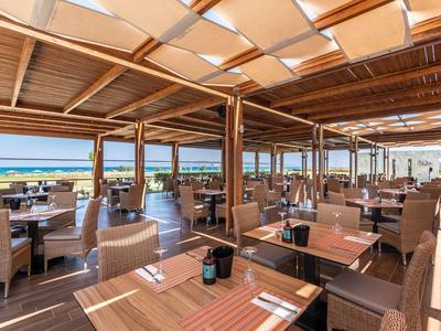 Covered restaurant overlooking the sea, furnished with wooden tables and comfortable chairs.