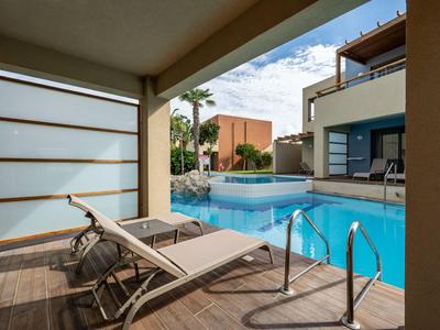 Modern pool area with lounge chairs, wooden plank flooring, and surrounding buildings under a blue sky.