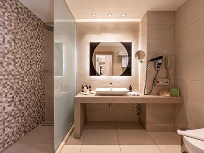 Bright bathroom with sink, large mirror, and modern shower featuring stone mosaic wall.