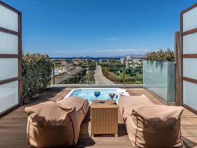 View from a terrace with two bean bags and a small table overlooking a pool and the sea in the background.