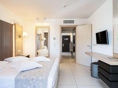 Bright hotel room with double bed, wall-mounted TV, and mirror next to the door.