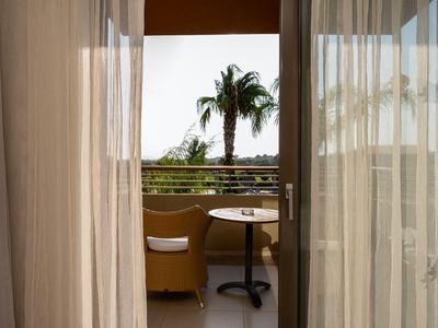 Balcony with chair and table, view of a palm tree and the sea in sunlight.
