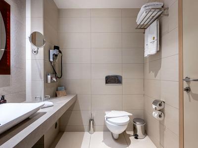 Modern hotel bathroom with sink, toilet, hairdryer, and towels on the wall.