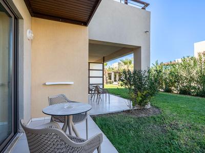 Terrace with table and chairs next to a garden and house facade under clear sky.