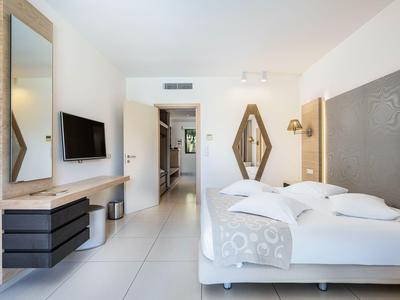 Modern bright hotel room with double bed, flat-screen TV, and large mirrors.