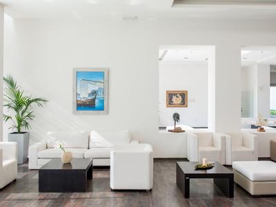 Bright modern lounge with white sofas, plants, and contemporary art on the wall.