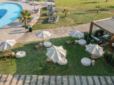View of a green terrace with seating cushions, umbrellas, and a nearby pool.