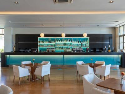 Modern hotel bar area with blue lighting, white chairs, and wooden flooring.