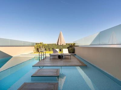 Modern outdoor pool with wooden walkways and umbrella on a hotel terrace under clear sky