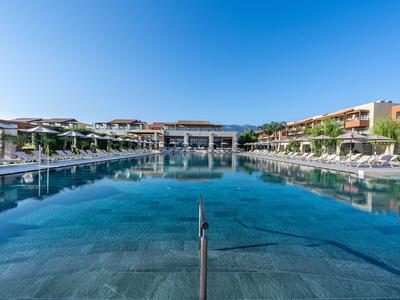 Large outdoor pool with sun loungers and hotel buildings under clear sky