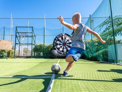 Ein Junge schießt auf einem Fußballplatz an einem sonnigen Tag einen Ball Richtung Tor.